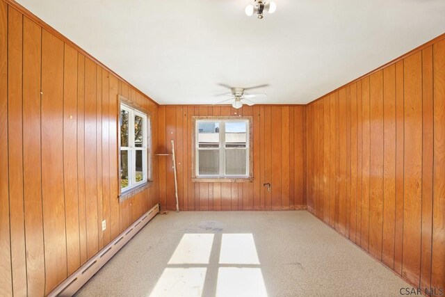 empty room featuring a baseboard radiator, light carpet, ceiling fan, and wood walls