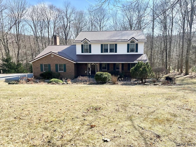 traditional-style home featuring brick siding, a front yard, covered porch, a chimney, and metal roof