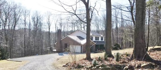 view of front of house with a forest view, gravel driveway, and a chimney