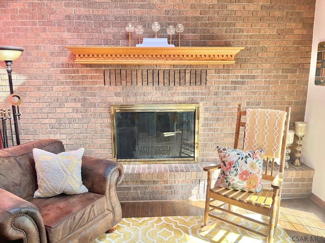 living room with a brick fireplace, wood finished floors, and brick wall