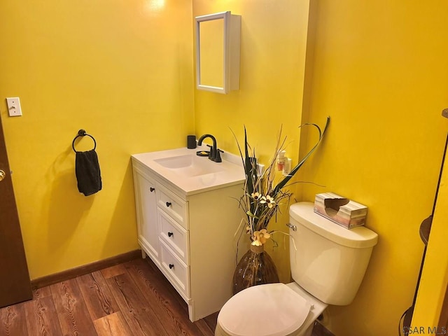 half bathroom featuring toilet, vanity, baseboards, and wood finished floors