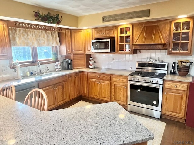 kitchen with light stone countertops, a sink, stainless steel appliances, custom range hood, and backsplash