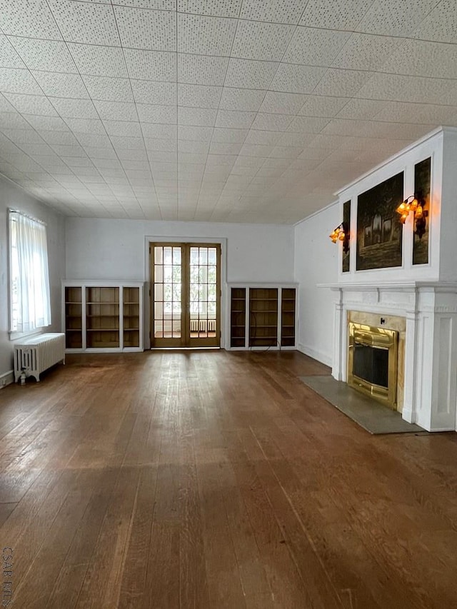 unfurnished living room featuring hardwood / wood-style floors, radiator heating unit, and french doors