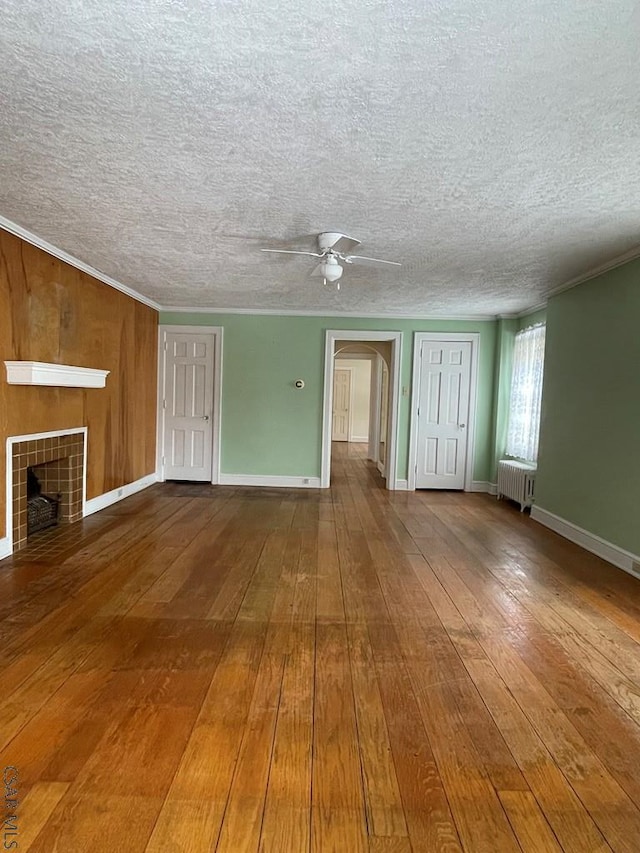 unfurnished living room with crown molding, wood-type flooring, radiator, a tile fireplace, and ceiling fan