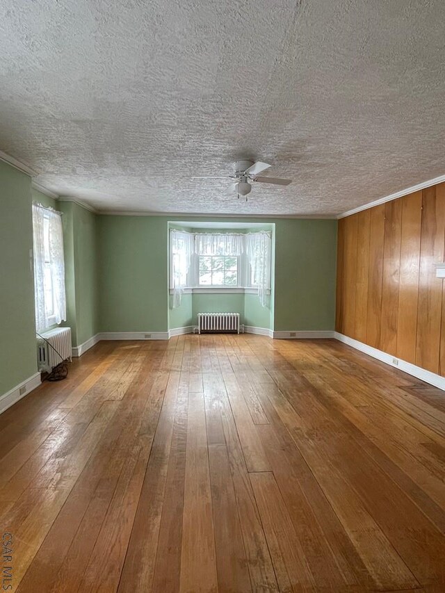 spare room featuring a healthy amount of sunlight, radiator, wooden walls, and wood-type flooring