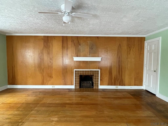 unfurnished living room featuring wood-type flooring, crown molding, a fireplace, and ceiling fan