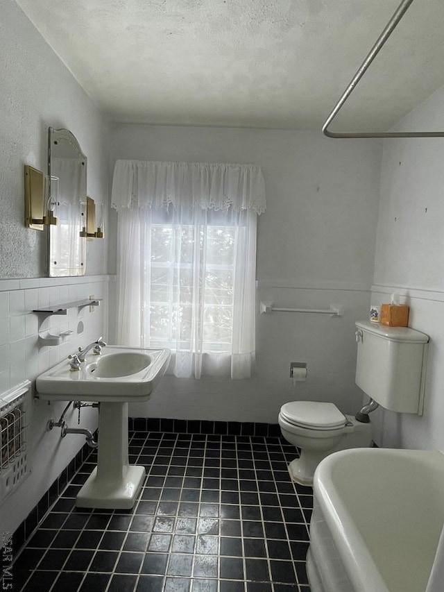 bathroom with a tub to relax in, a textured ceiling, tile patterned floors, and toilet