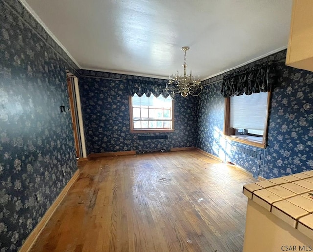 unfurnished dining area with crown molding, a chandelier, and hardwood / wood-style floors