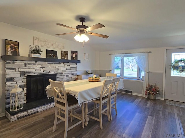 dining area featuring ceiling fan, a stone fireplace, and dark hardwood / wood-style flooring