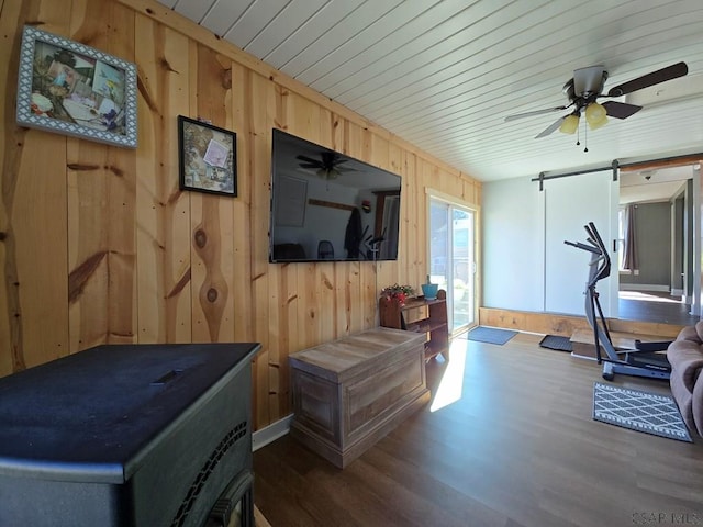 exercise room with a barn door, dark hardwood / wood-style floors, ceiling fan, and wood walls