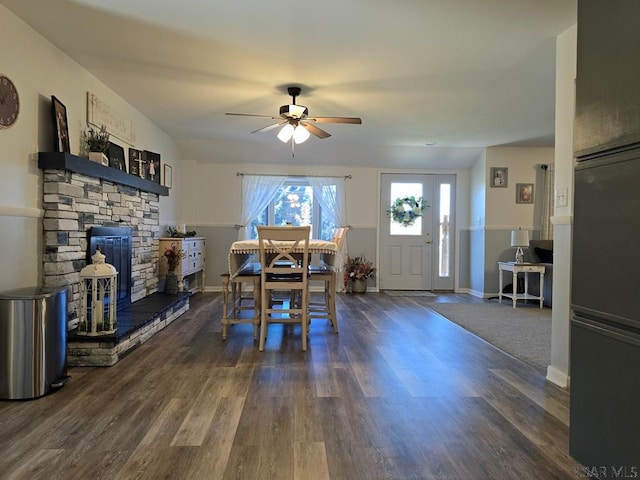 dining space featuring ceiling fan, dark hardwood / wood-style flooring, and a stone fireplace