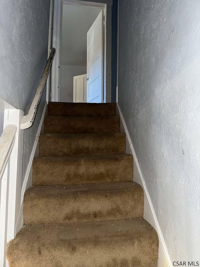 stairway featuring a textured wall and baseboards