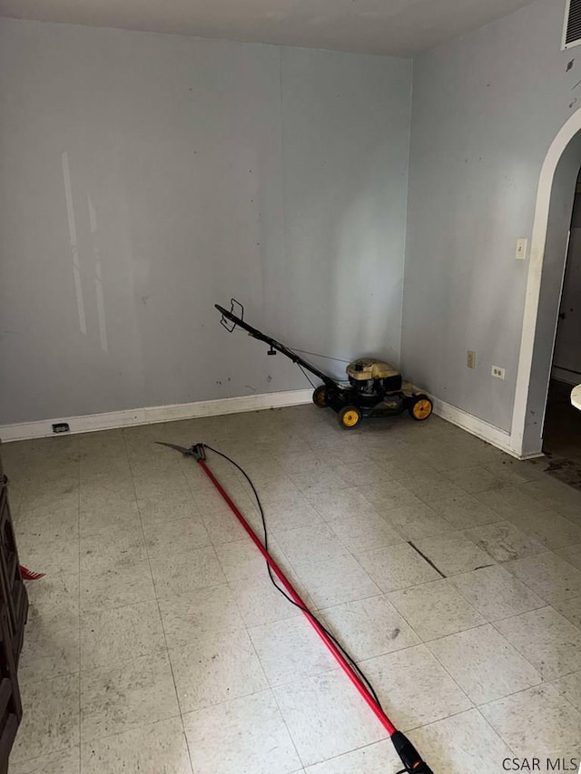 spare room featuring arched walkways, light floors, visible vents, and baseboards