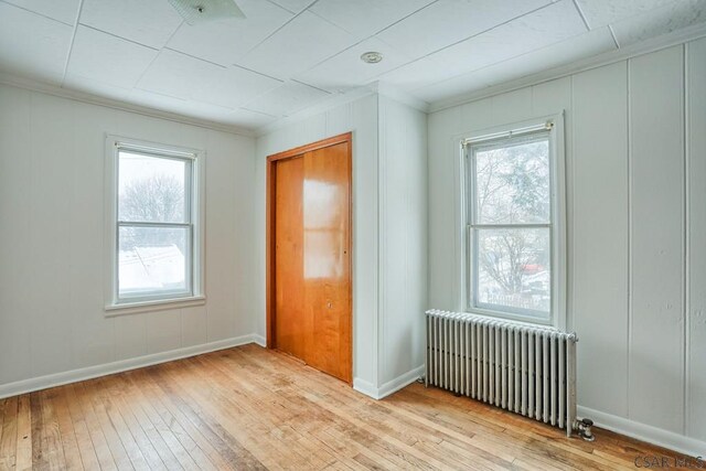 empty room with ornamental molding, radiator, and light hardwood / wood-style flooring