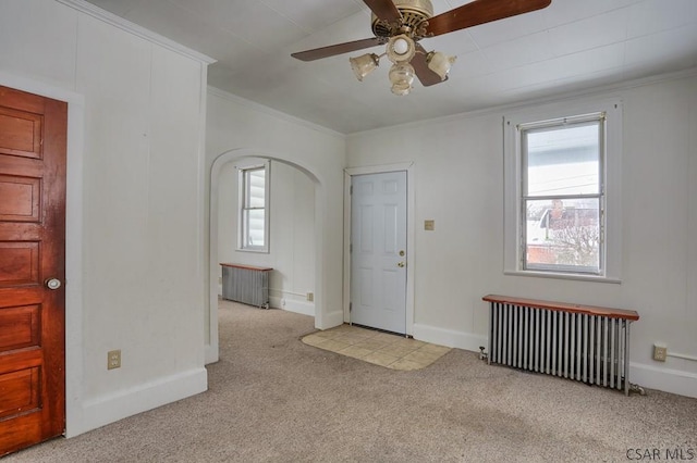 foyer with ceiling fan, light colored carpet, crown molding, and radiator