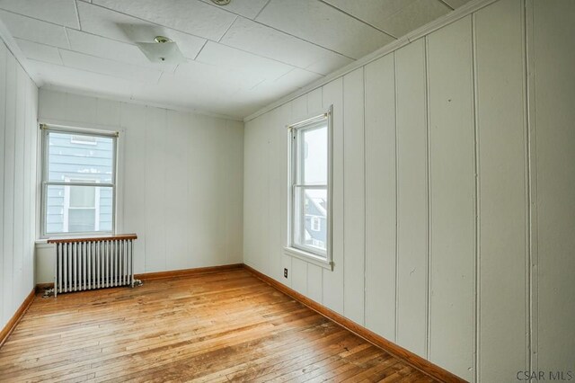 empty room with crown molding, radiator heating unit, and light hardwood / wood-style flooring