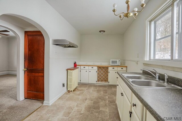 kitchen featuring plenty of natural light, range hood, sink, and white cabinets