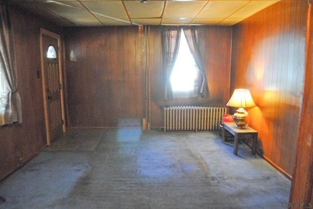 carpeted spare room featuring radiator and wood walls