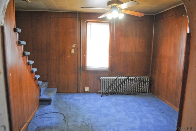 entryway featuring carpet, radiator, ceiling fan, and wood walls