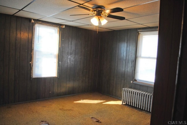 unfurnished room featuring radiator heating unit, wooden walls, plenty of natural light, and carpet flooring