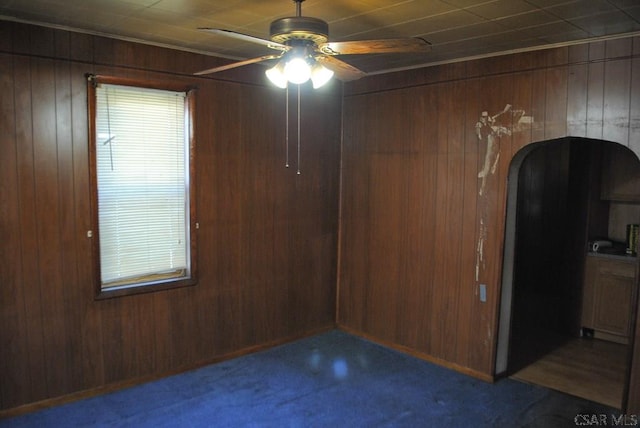 carpeted empty room featuring wooden walls and ceiling fan