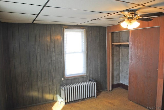 bedroom featuring a paneled ceiling, radiator heating unit, wooden walls, carpet flooring, and ceiling fan