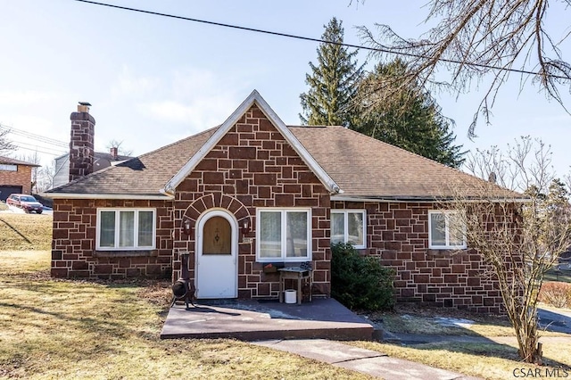 view of front of house featuring a shingled roof, a front yard, a chimney, a patio area, and stone siding