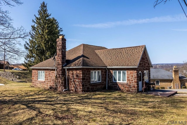 view of side of home featuring a yard, stone siding, roof with shingles, and a chimney