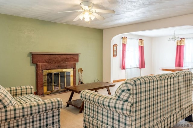 carpeted living room featuring arched walkways, a glass covered fireplace, and ceiling fan with notable chandelier