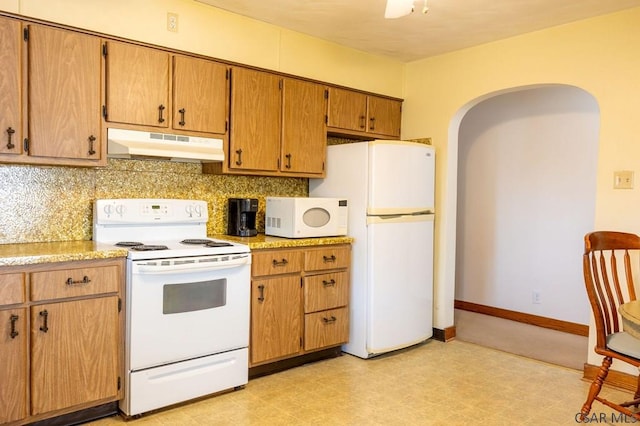 kitchen featuring white appliances, arched walkways, decorative backsplash, light countertops, and under cabinet range hood