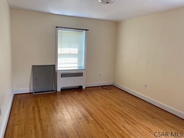 empty room with light hardwood / wood-style flooring and radiator heating unit