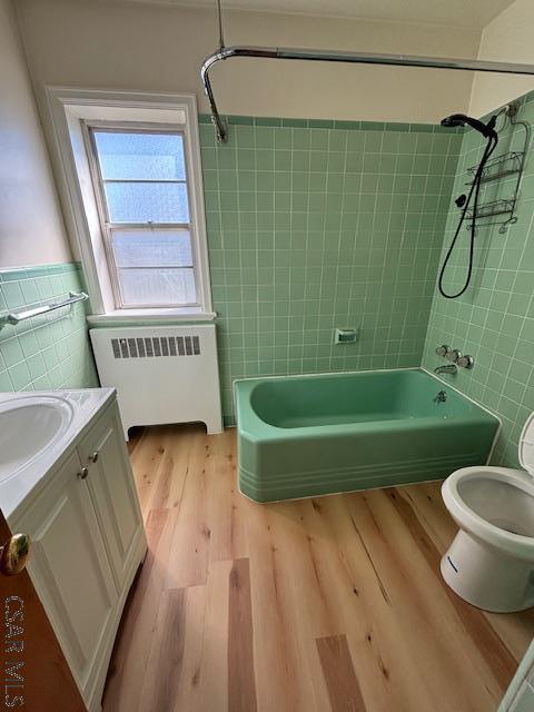 full bathroom with tile walls, radiator heating unit, vanity, tiled shower / bath combo, and hardwood / wood-style flooring