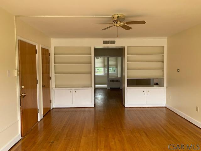 unfurnished room featuring ceiling fan, radiator, dark hardwood / wood-style floors, and built in shelves