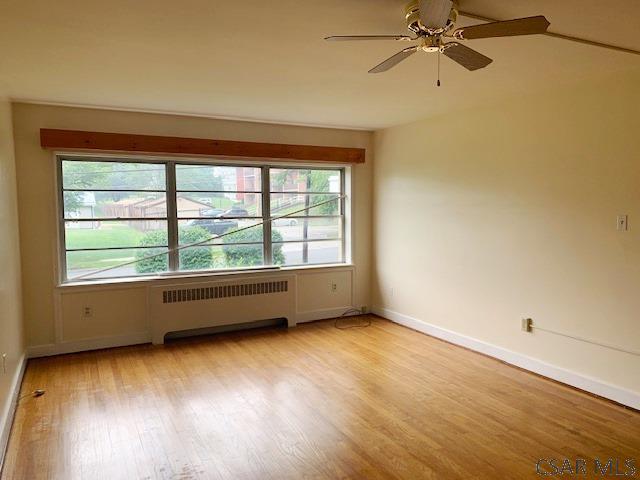 empty room featuring ceiling fan, radiator, and light hardwood / wood-style floors