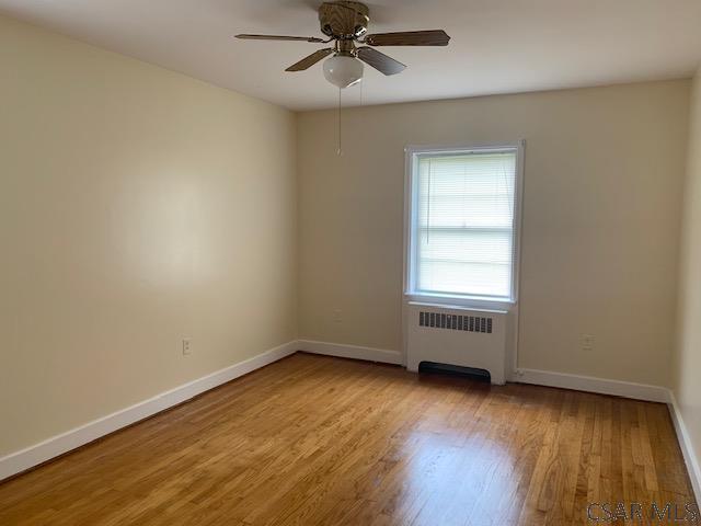 empty room featuring ceiling fan, radiator, and light hardwood / wood-style floors