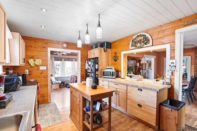 kitchen with black refrigerator, hanging light fixtures, light hardwood / wood-style floors, light brown cabinetry, and wood walls