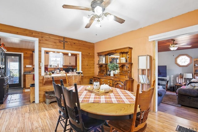 dining space with ceiling fan, light wood-type flooring, and wood walls