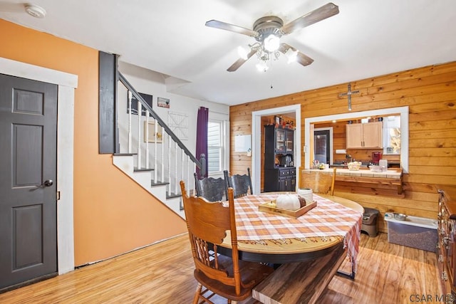 dining space featuring ceiling fan, light wood-type flooring, and wood walls