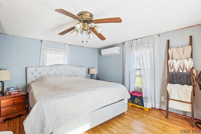 bedroom with ceiling fan, light hardwood / wood-style floors, multiple windows, and an AC wall unit