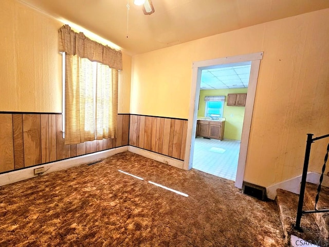 carpeted empty room with visible vents, a wainscoted wall, and wood walls