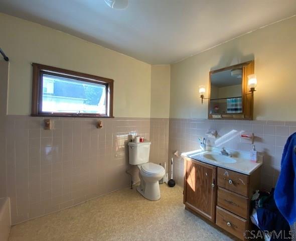 bathroom featuring vanity, toilet, and tile walls