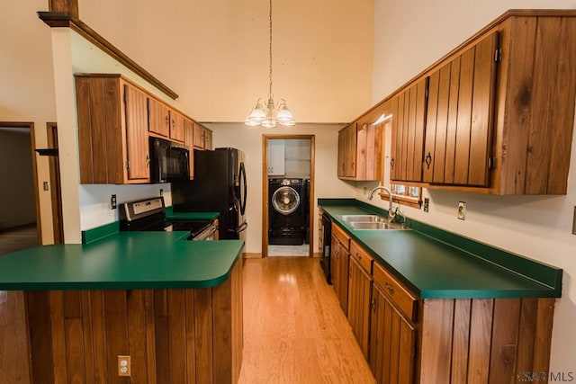 kitchen featuring washer / dryer, sink, hanging light fixtures, black appliances, and light wood-type flooring