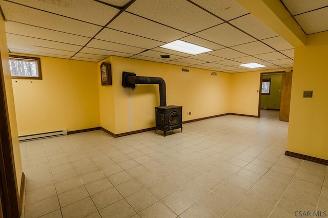 basement featuring a wood stove, a paneled ceiling, and baseboard heating