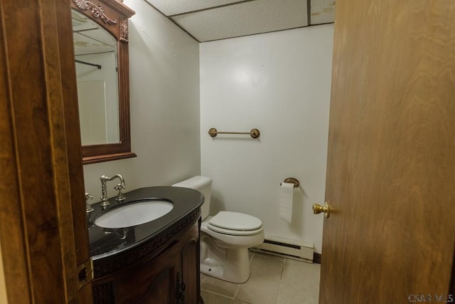 bathroom with tile patterned flooring, a baseboard heating unit, vanity, a drop ceiling, and toilet