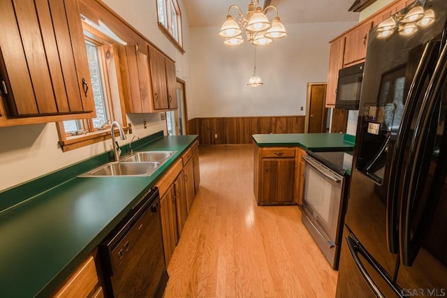 kitchen featuring sink, wood walls, hanging light fixtures, light wood-type flooring, and black appliances