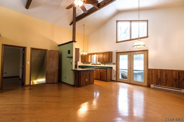 unfurnished living room featuring ceiling fan, vaulted ceiling with beams, wooden walls, wood-type flooring, and a baseboard radiator