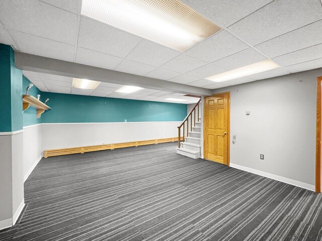 basement with baseboard heating, a paneled ceiling, and dark colored carpet