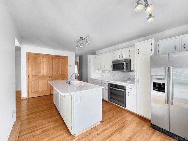 kitchen with sink, a kitchen island with sink, hanging light fixtures, stainless steel appliances, and white cabinets