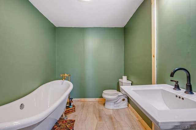 bathroom with a soaking tub, baseboards, a sink, and toilet