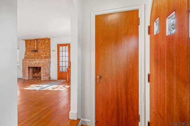 hallway featuring arched walkways, wood finished floors, and baseboards